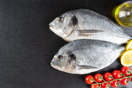Fresh fish dorado on black slate background with ingredients for cooking