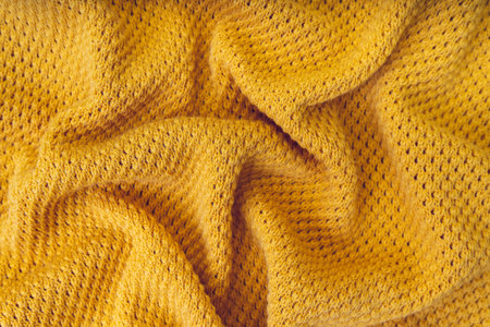 Yellow color crumpled knitting wool texture. Close up background of knitted fabric with dots pattern