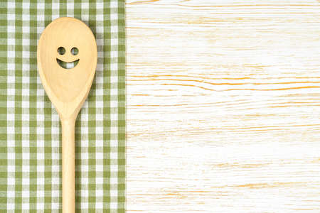 Wooden spoon with smile on green checkered tablecloth on white wooden surface. Mockup for menu or recipe, restaurant, website with cooking. Kitchen food background, template, flat lay with copy spaceの写真素材