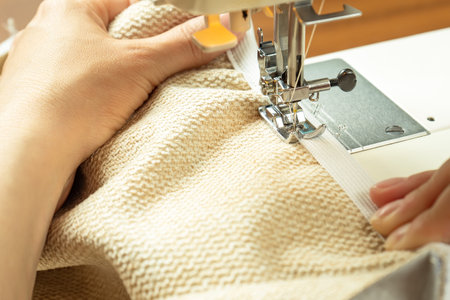 Seamstress hands holding white textile fabric. Female hands stitching white fabric on modern sewing...
