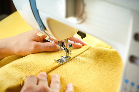 Female hands stitching yellow fabric on modern sewing machine. Close up view of sewing process.の写真素材
