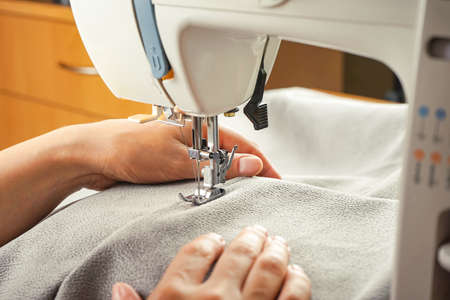 Female hands stitching gray fabric on modern sewing machine. Close up view of sewing process.の写真素材