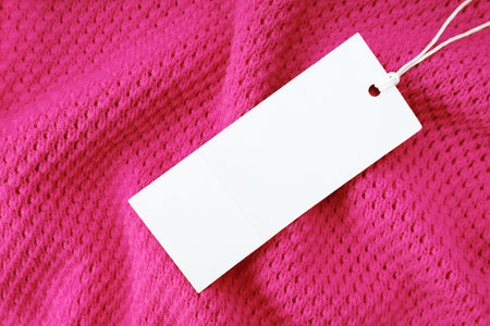 White blank rectangular clothing tag on pink knitted fabric background. Shopping, sale, discount...