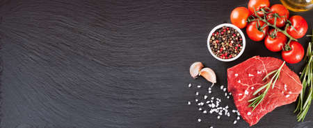 Raw beef steak with spices and ingredients for cooking on black slate background. Banner for restaurant menu, header for web sites. Top view, flat lay, mockup with copy space for textの写真素材