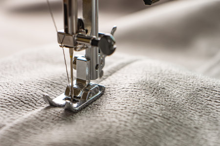 Modern sewing machine presser foot with gray fabric and thread, closeup, copy space. Sewing process...