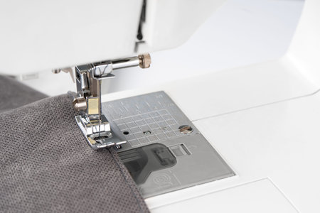 Modern sewing machine presser foot with gray fabric and thread, closeup. Sewing process clothes,...