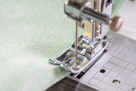 Modern sewing machine presser foot with green fabric and thread, closeup, macro. Sewing process...