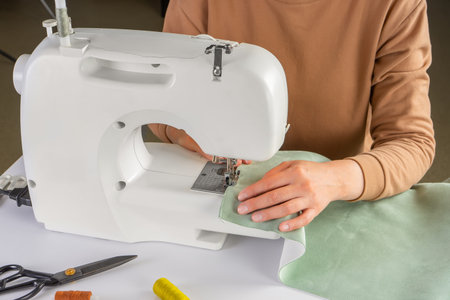 Female hands stitching green fabric on modern sewing machine at workplace in atelier. Women's hands...