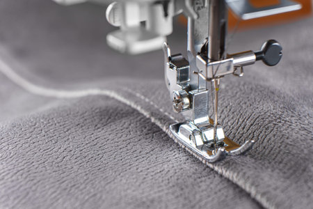 Modern sewing machine with gray velours fabric. Sewing process clothes, curtains upholstery....