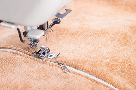Modern sewing machine special presser foot with beige corduroy fabric and thread, closeup. Sewing...