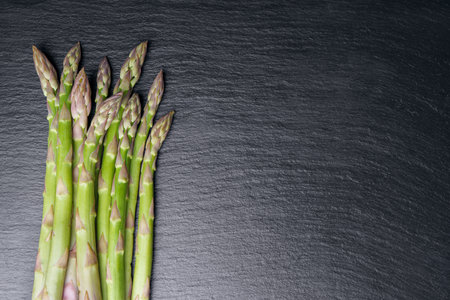 Bunch of fresh green asparagus on black slate background. Edible sprouts, stems of sparrowgrass. Healthy food, fresh vegetable, ingredient for cooking Top view, banneer, header with copy spaceの写真素材