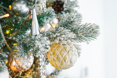Snowy frosted Christmas tree branch with festive lights and decorative gold and silver ornaments close up. Holiday spirit with shimmering decorations and warm lights. Wallpaper, backdrop, backgroundの写真素材