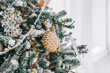 Snowy frosted Christmas tree branch with festive lights and decorative gold and silver ornaments close up. Holiday spirit with shimmering decorations and warm lights. Wallpaper, backdrop, backgroundの写真素材