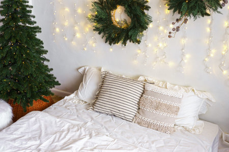 Christmas tree and wreath in bedroom, holiday decor and warm lighting during winter months. Bed with...