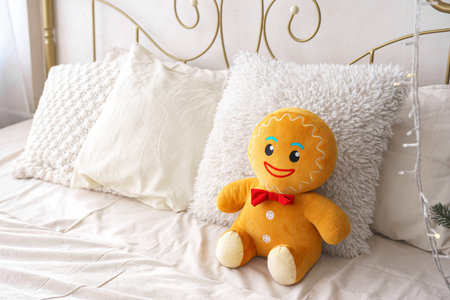 Christmas gingerbread plush toy seated on bed surrounded by fluffy pillows in bright, inviting...