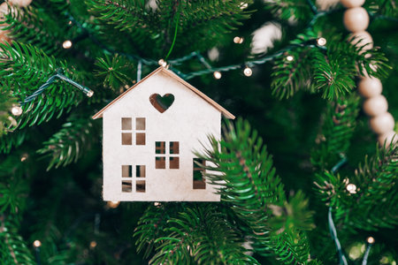 Handcrafted wooden house ornament with heart shaped cutout hanging on Christmas tree branch with warm lights background, creating a festive atmosphere of winter holidays. Wallpaper, backdropの写真素材