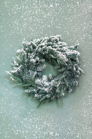 Beautifully crafted winter Christmas wreath made of evergreen branches on green background with snow. Festive ornament, decor for winter holidaysの写真素材