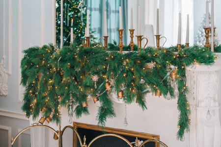 Beautifully decorated mantel is adorned with lush greenery garland with twinkling lights and golden candle holders with candles. Festive Christmas atmosphere, perfect for winter holiday season.の写真素材