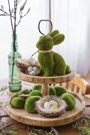 Green moss Easter Bunny and decorative Easter eggs in nest on on a two tiered wooden plate in home...