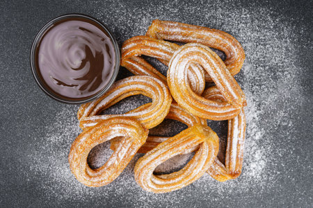Traditional spanish dessert churros, fried dough pastry dusted with powdered sugar and chocolate on black background. Street food, sweet snack, homemade dessert. Top view, flat layの写真素材
