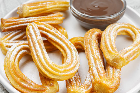 Traditional spanish dessert churros, fried dough pastry dusted with powdered sugar and chocolate...