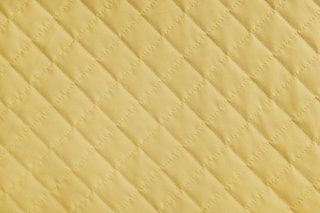 Checkered, diamond stitching pattern, yellow quilted fabric background. Blanket or puffer jacket, stitch rhombus texture close up, macro. Wallpaper, backdrop.の写真素材