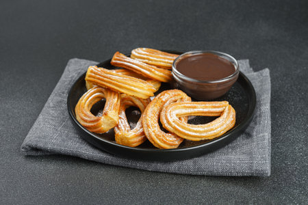 Traditional spanish dessert churros, fried dough pastry dusted with powdered sugar and chocolate sauce on black background. Street food, sweet snack, homemade dessert.の写真素材