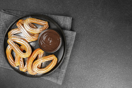 Traditional spanish dessert churros, fried dough pastry dusted with powdered sugar and chocolate sause on black background. Street food, sweet snack, homemade dessert. Top view, copy spaceの写真素材
