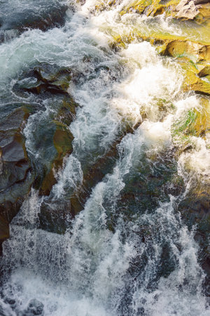 Dynamic image of a fast flowing mountain waterfall, rapid river crashing over mossy rocks. Energy and beauty of natural water features in pristine forested environments. Abstract natural backgroundの写真素材