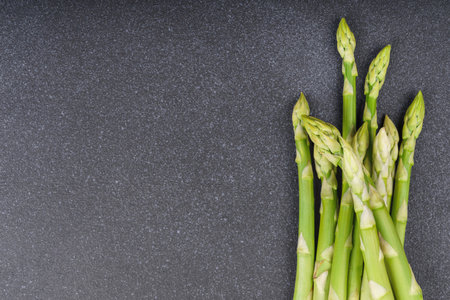 Bunch of raw fresh green asparagus stalks macro, close up on black textured background with copy space. Healthy food, fresh produce, cooking ingredient, vegetarian recipe, organic agriculture.の写真素材