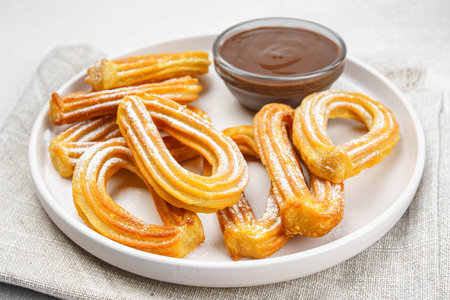 Traditional spanish dessert churros, fried dough pastry dusted with powdered sugar and chocolate sause on white background. Street food, sweet snack, homemade dessert. Top view, copy spaceの写真素材
