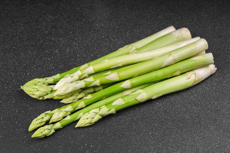 Bunch of raw fresh green asparagus stalks on dark black textured background. Healthy food, fresh produce, cooking ingredient, vegetarian recipe, or organic farming, agriculture.の写真素材