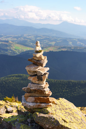 Carefully balanced cairn made of flat rocks on Carpathian mountaintop with forested ridges and distant valleys in background. Symbol of travel and hiking exploration, calm, silence and balanceの写真素材