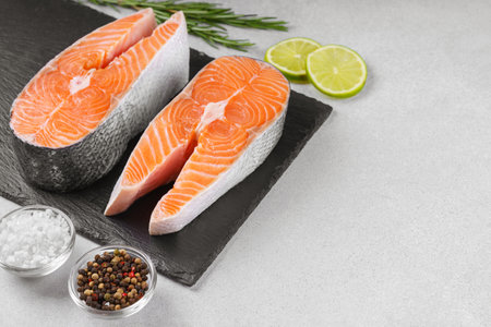 Two fresh raw salmon steaks on white stone surface with food ingredients. Tomatoes, lime, rosemary, salt, and pepper. Healthy eating, seafood, cooking, recipe and menu concepts. Top view, copy spaceの写真素材