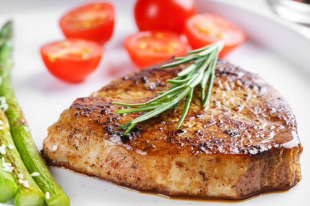 Close up, macro of tasty grilled beef steak served with green asparagus and cherry tomatoes on white plate, with cutlery. Perfect for food menu, diet, or culinary design concepts.の写真素材