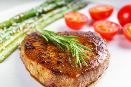 Close up, macro of tasty grilled beef steak served with green asparagus and cherry tomatoes on white plate, with cutlery. Perfect for food menu, diet, or culinary design concepts.の写真素材