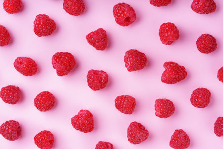 Scattered ripe red raspberries on pastel pink background. Flat lay, top view. Colorful minimal food composition, food design. Perfect for healthy eating and summer fruit, harvest concepts.の写真素材