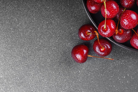 Close up of black plate filled with ripe red sweet cherry placed on gray linen napkin on dark...