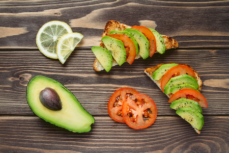 wheaten toasts with avocado and tomato slices and pepper on a wooden background. ?oiety avocado, lemon slices. Shooting angle of 90 degrees.の写真素材