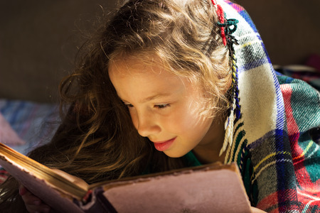 portrait of cute curly school girl reading an old book at cold dayの写真素材