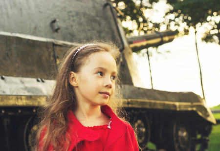 Toned  portrait of little girl near military tank at sunsetの写真素材