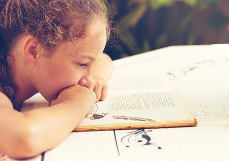 Toned Outdoor portrait of a cute little girl reading a bookの写真素材