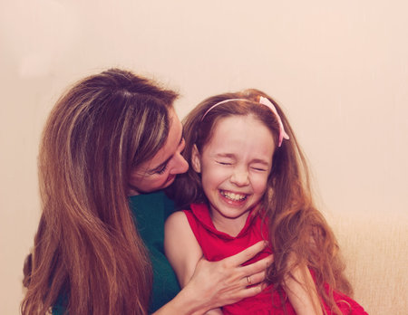 Motherhood is pure joy. Beautiful young woman hugging little girl, smiling and looking at her with love. Mother and daughter having fun togetherの写真素材