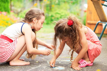 Summer, childhood, leisure and people concept - happy little Girls is drawing with chalks on summer parkの写真素材