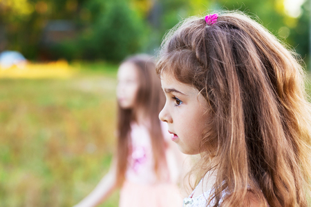 Beautiful little girl with long curly hair, looking worried at summer day.  Place for textの写真素材