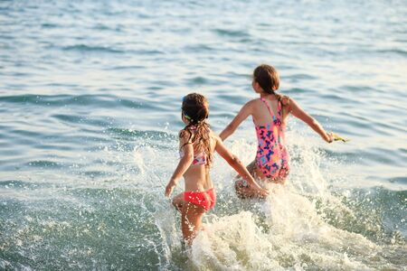Two Cute Little Girls playing with waves by the Sea at sunset.  Summer Sunny Day, Ocean Coast, happy Kids concept,  soft focusedの写真素材