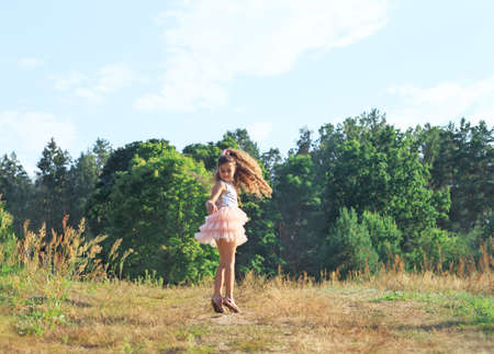 Beautiful little girl dancing with flowers in sunny spring park. Happy cute kid having fun outdoors at sunset.の写真素材