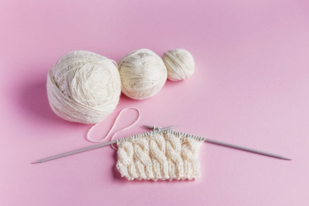 White balls of thread with knitting needles in a string bag on a lilac background for knitting warm...