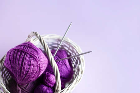 Purple lilac balls of thread with knitting needles in a basket on a lilac background for knitting warm clothes, hobbiesの写真素材