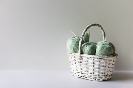 Light green yarn threads in a white basket on a gray background with knitting needles.の写真素材